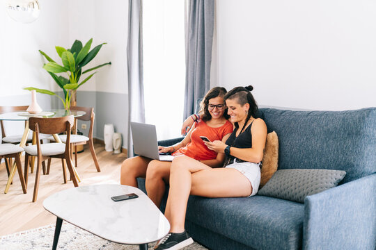 Girlfriends using laptop and text messaging on smart phone at home