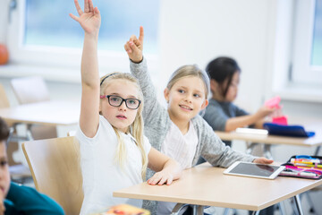 Schoolgirls with tablet raising their hands in class