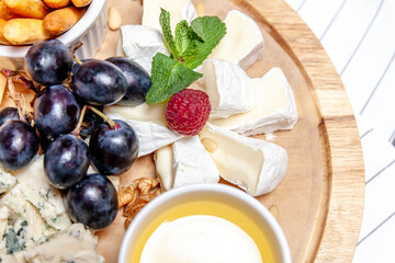 Board with different types of cheese. Cheeses mix set dor blu chedar parmesan brie honey sauce finger bread and grape on wooren palte. Restaurant menu breakfast plate. Healthy snack assortment.