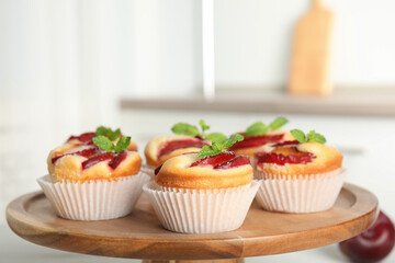 Delicious sweet cupcakes with plums on wooden stand, closeup