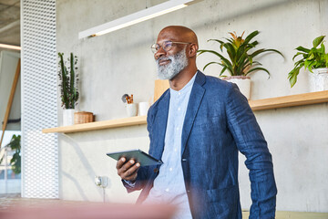 Smiling man looking away while holding digital tablet standing at home