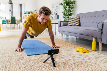 Young man looking at mobile phone while exercising on mat at home