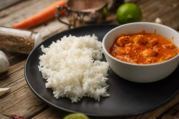 Tasty chicken curry with boiled rice on rustic wooden table with spices background. Dinner with traditional Indian dish. Exotic delicious. Food concept.