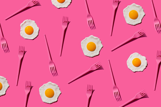 Pattern of pink plastic forks and fried eggs against pink background