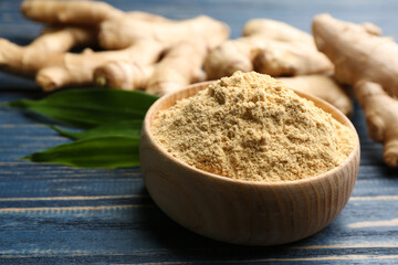 Dry ginger powder in bowl and fresh root on blue wooden table