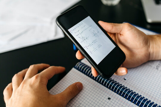 Hands of male adult student holding smart phone with mathematical equation at home