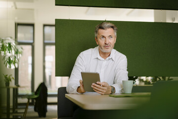 Businessman using digital tablet while sitting by table at cafeteria