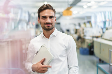 Confident young male engineer holding digital tablet while standing at illuminated factory