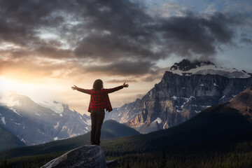 Girl enjoying the beautiful scenery of the Canadian Rockies. Dramatic Colorful Sunrise Sky. Taken on Icefields Parkway, Banff, Alberta, Canada.