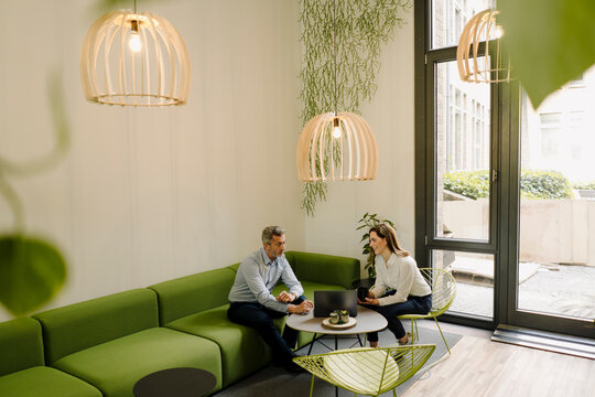 Business people working on laptop while sitting on sofa at office