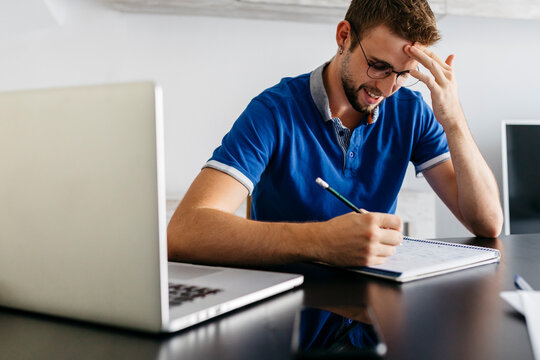 Smiling handsome man reading from book while sitting with laptop at home