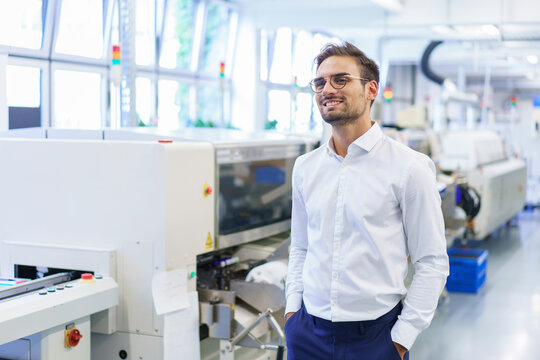 Smiling young male technician standing with hands in pockets at illuminated factory