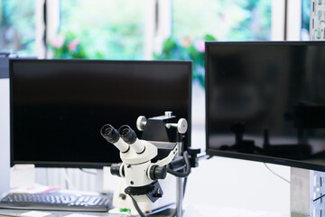 White microscope against computer monitors at illuminated laboratory
