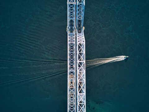 Aerial view of boat moving over Volga River under metallic railway bridge