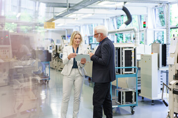 Confident businesswoman discussing over digital tablet with senior businessman in factory