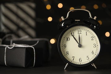 Vintage alarm clock with decor on black table against blurred Christmas lights, closeup. New Year...