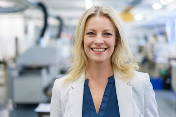 Smiling mature blond female professional standing at illuminated industry
