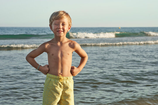 Smiling boy with hand on hip standing against sea at beach