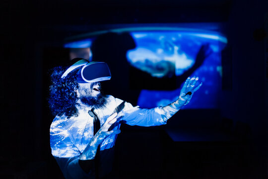 Playful man with virtual reality glasses standing in dark at home during pandemic