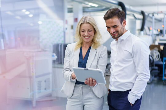 Smiling blond businesswoman discussing over digital tablet with young male colleague at factory