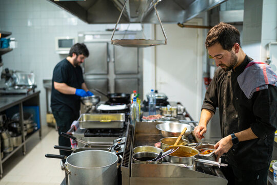 Chef standing by kitchen counter with coworker cooking in background at kitchen