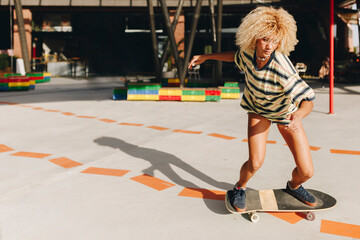 Confident blond woman skateboarding on footpath during sunny day