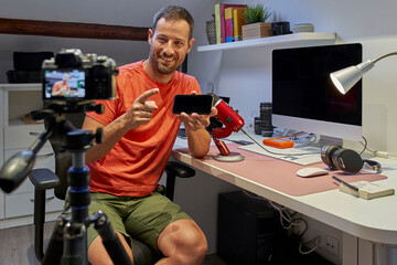 Mid adult man holding smart phone while video recording from home