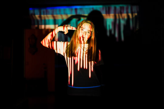 Woman showing gun hand sign on head while standing in light reflection at home during pandemic