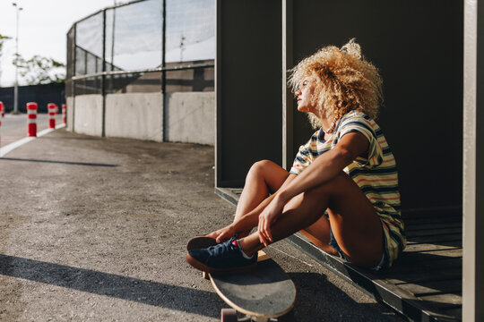Thoughtful woman sitting with skateboard while looking away on sunny day