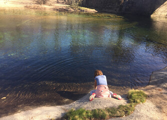 rear view of girl sitting on rock by river
