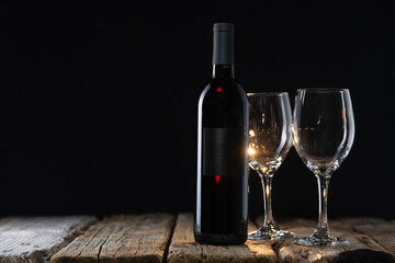 Dark bottle of expensive red wine and glasses on wooden table on black background. Concept of advertising and promotion. Space for text.