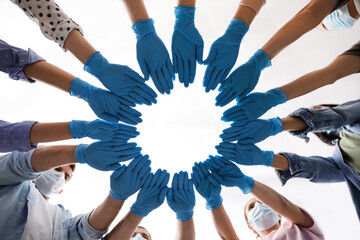 People in blue medical gloves joining hands on light background, low angle view