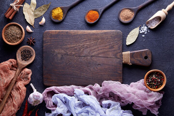 Cutting board with spices and herbs for cooking meat on dark background