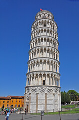 The Leaning Tower of Pisa seen from the ground level. The tower has both symmetry and intricately woven elements of arches and columns accenting its unique beauty.