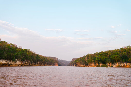Fisherman on rowboat in moody river sorrounded by jungle and rocky landscape