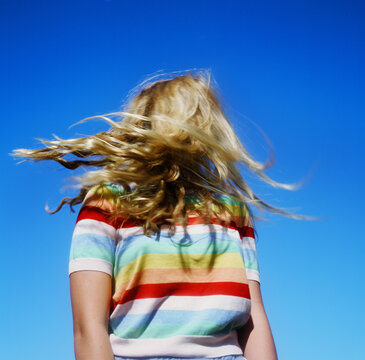 blonde teenage girl in rainbow sweater against bright blue sky