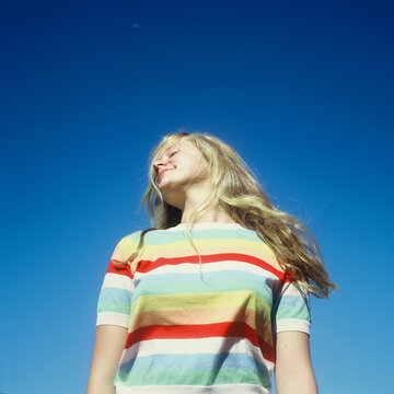 blonde teenage girl in rainbow sweater against bright blue sky