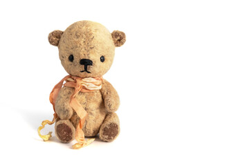 Vintage handmade teddy bear with a ribbon around the neck sits on a white background. Close-up. Copy space.