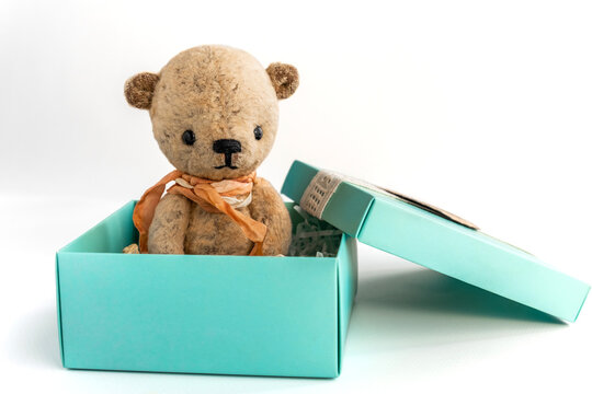 Small vintage handmade teddy bear sits in a gift box on a white background. Gift for an important holiday. Copy space.