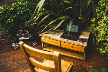 an outside work station including desk, chair, laptop and surrounded by wooden terrace and green plants