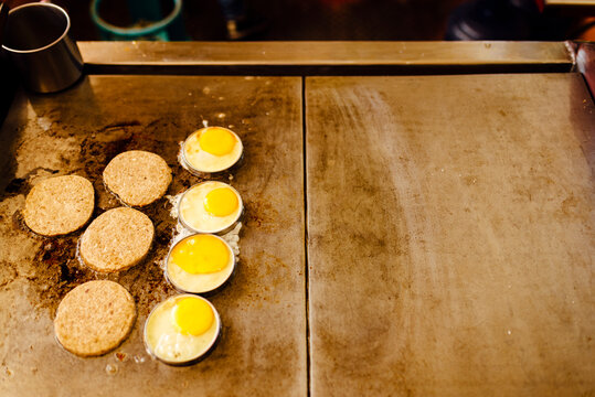 Row of burger meat and eggs frying in cooking plate