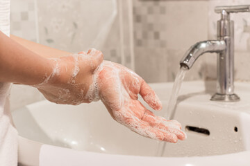 Female washes his hands with soap over a sink in the bathroom. Concept of hygiene treatment.