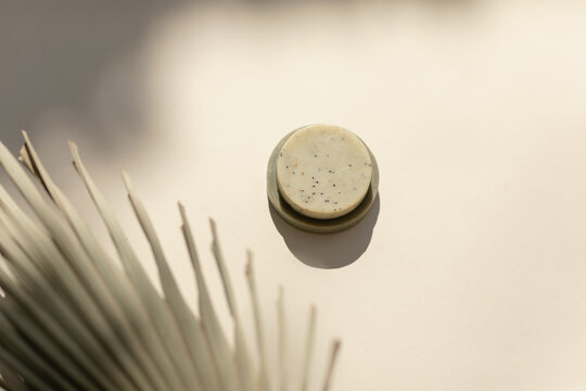 minimal still life of natural soap with palm leaf in dappled light on cream background