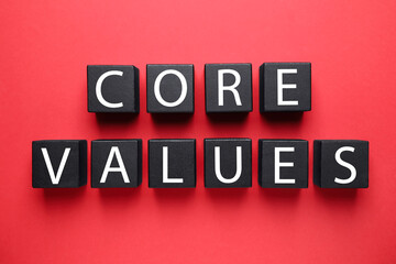 Black wooden cubes with phrase CORE VALUES on red background, flat lay