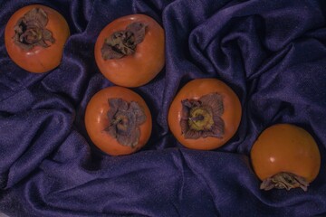 Scattered orange fresh persimmon fruits on a dark blue wrinkled cloth