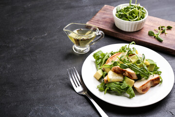 Delicious salad with chicken, lemon and arugula on black table. Space for text