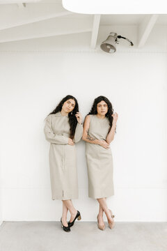 two women wearing matching outfits with white background and same body language