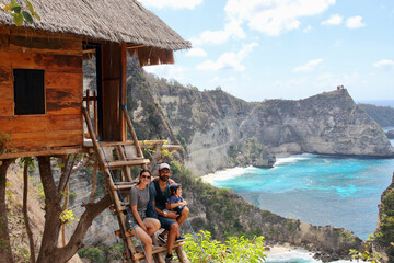 Parents and little kid enjoying the views from the wooden stairs of one of the famous treehouses in Thousand Islands Viewpoint, on of the most amazing spots in Nusa Penida Island, Indonesia, Bali.