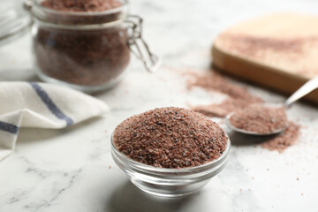 Ground black salt in glass bowl on white marble table. Space for text