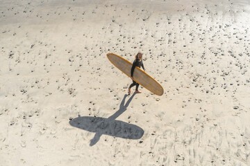 view from above of man holding yellow surfboard on sunny beach day